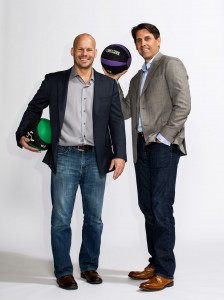 Two men dressed in semi formal clothing holding medicine balls with white backdrop