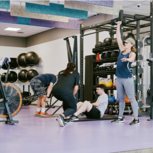 Person doing rows, one person doing core with personal trainer, and another person lifting a dumbbell